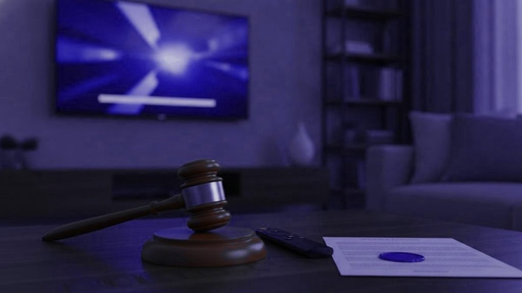 Wooden gavel, a TV remote and a document with a wax seal on a table in a living room with the television switched on